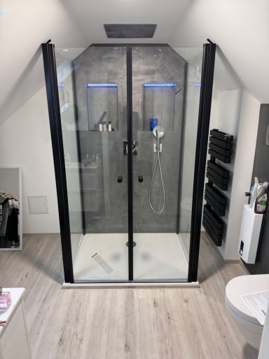 Dusche mit gläsernen Türen, moderner Ausstattung und hellen Fliesen.