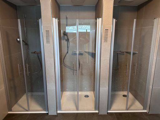 Drei moderne Duschkabinen mit Glastüren in einem stilvollen Badezimmer.