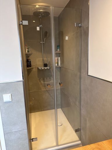 Moderne Dusche mit Glastür und grauen Wänden, sauber und hell.