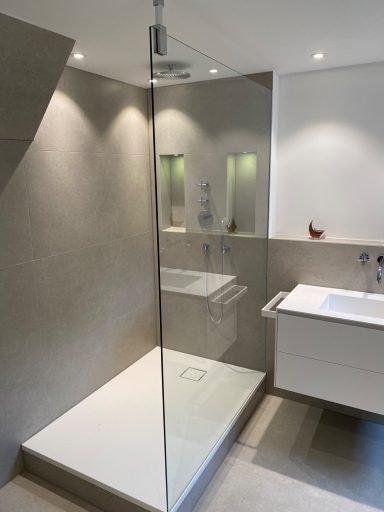 Moderne Dusche mit Glasschleuse, helle Wände und minimalistischer Waschbeckenanlage.